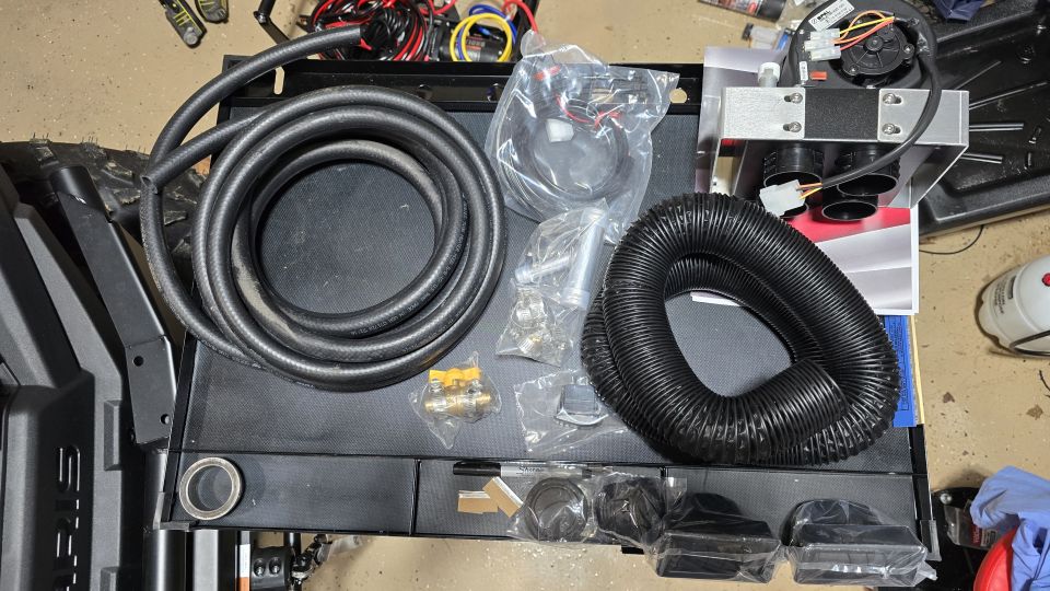 Parts for a vehicle heater kit laid out on a surface, including hoses, a fan unit, and various connectors