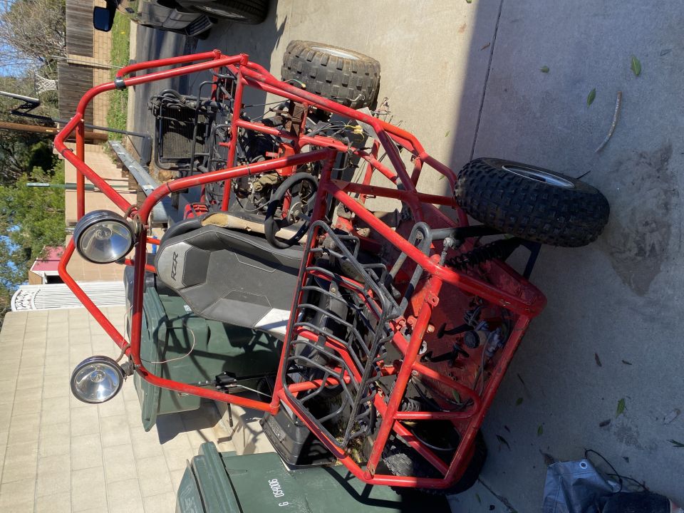 Red off-road buggy with roll cage, two seats, and off-road tires, parked on a driveway