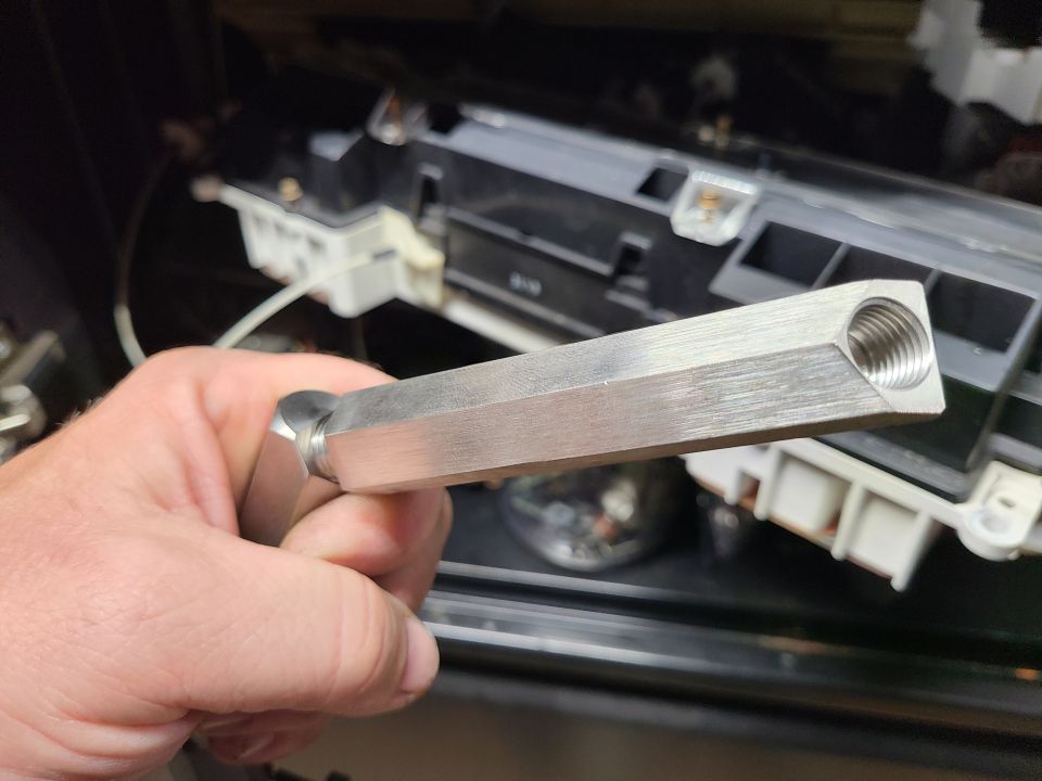 Hex wrench with a threaded opening on one end, held in front of a car's dashboard components