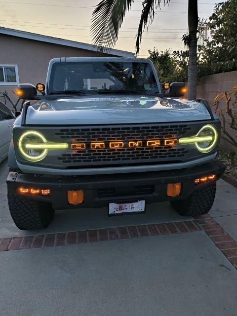 2023 Ford Bronco - The front of a Ford Bronco is shown with its grille illuminated and headlights on.