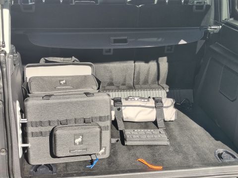 2023 Ford Bronco - The cargo area of a vehicle contains multiple storage bags, including a large gray bag with MOLLE webbing and a smaller pouch, and a rolled…