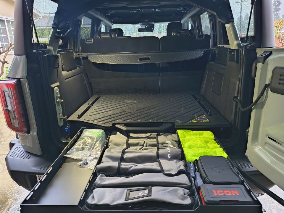 Back of a Ford Bronco with cargo drawers pulled out, showing storage bags and a neon green towel