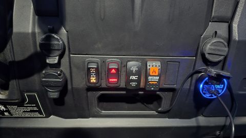 2025 Polaris RANGER - Close-up of a UTV's dashboard showing various control switches and power outlets, including a glowing blue USB charger.