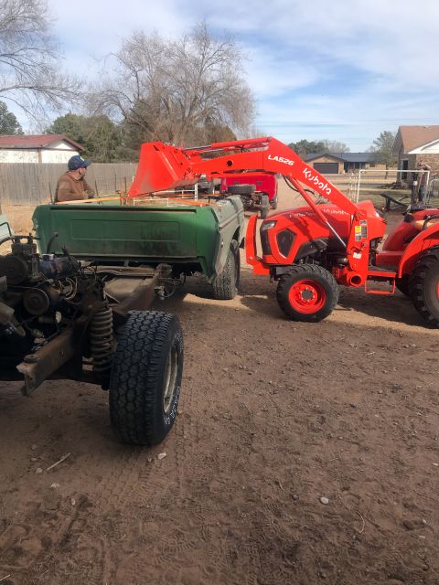 1994 Ford Bronco - A Kubota tractor lifts a green pickup truck bed as a person watches.