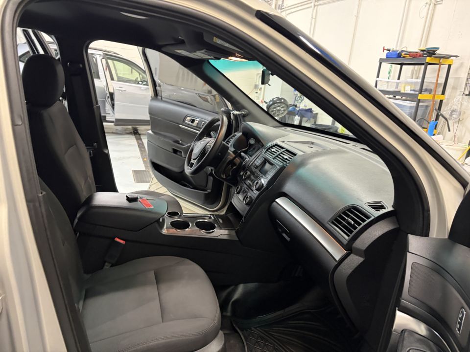 Interior of a silver SUV, showing front seats, dashboard, and steering wheel. Another silver SUV is visible through the open door