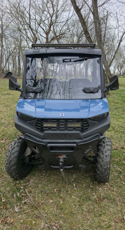 2025 Polaris RANGER - A blue Polaris utility vehicle is parked outdoors on a grassy area with trees in the background.