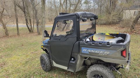 2025 Polaris RANGER - A side-by-side utility vehicle, identified as a RANGER SP, is parked on a grassy area with trees in the background.