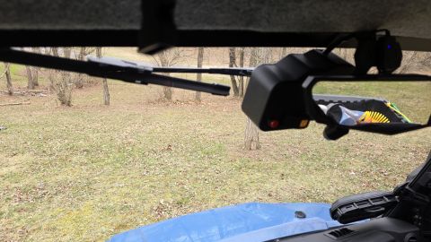 2025 Polaris RANGER - View from inside a vehicle shows a side mirror and windshield wiper assembly, with a wooded area in the background.