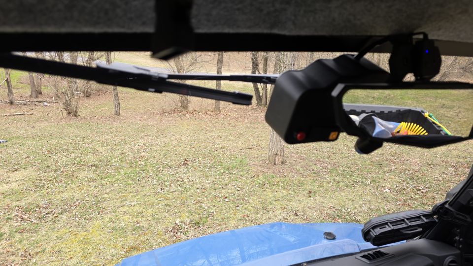 Side mirror and windshield wiper assembly inside a vehicle, with a blue tarp visible on the hood