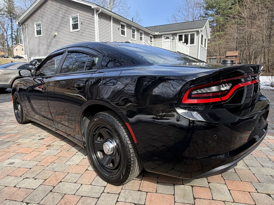 Black Dodge Charger police car parked on brick driveway, another car visible to the left