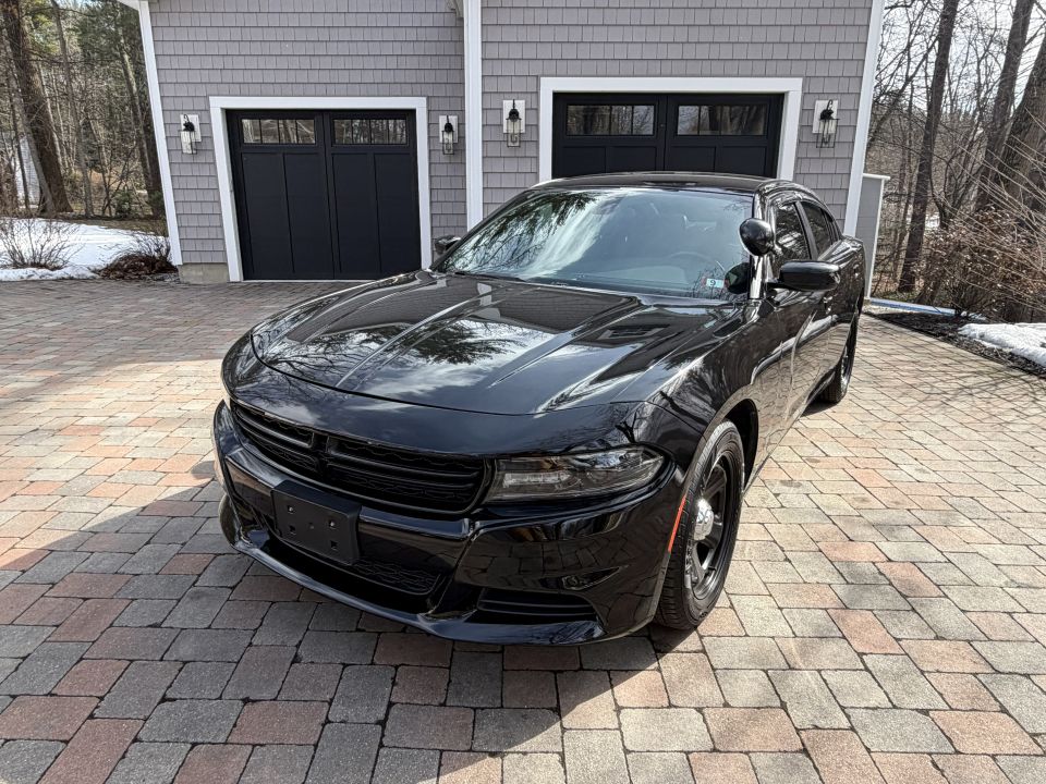Black police car parked on a paver driveway in front of a gray house with black garage doors