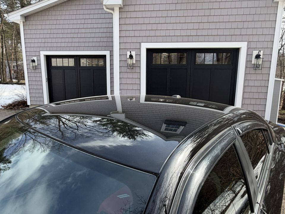 Black car roof and side window reflecting a garage
