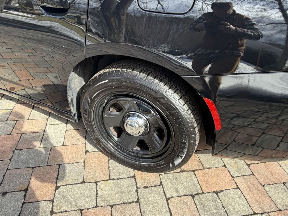 Black car rear wheel with a black steel wheel and chrome hubcap, parked on a paver driveway