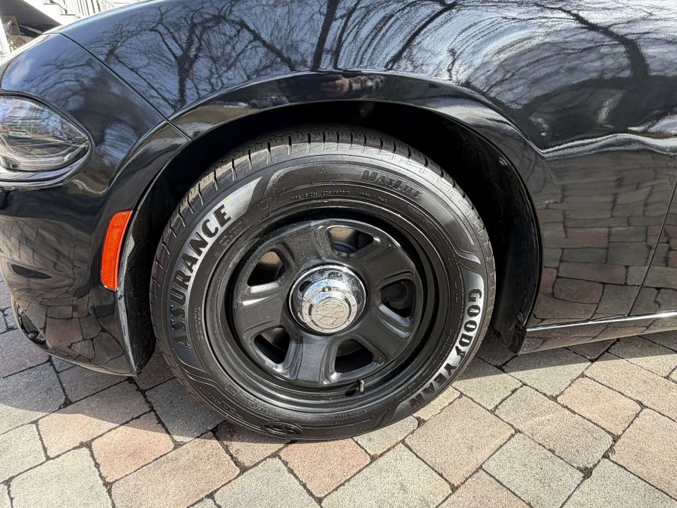 Close-up of a black car's front tire with Goodyear Assurance lettering and a black steel wheel with a chrome center cap
