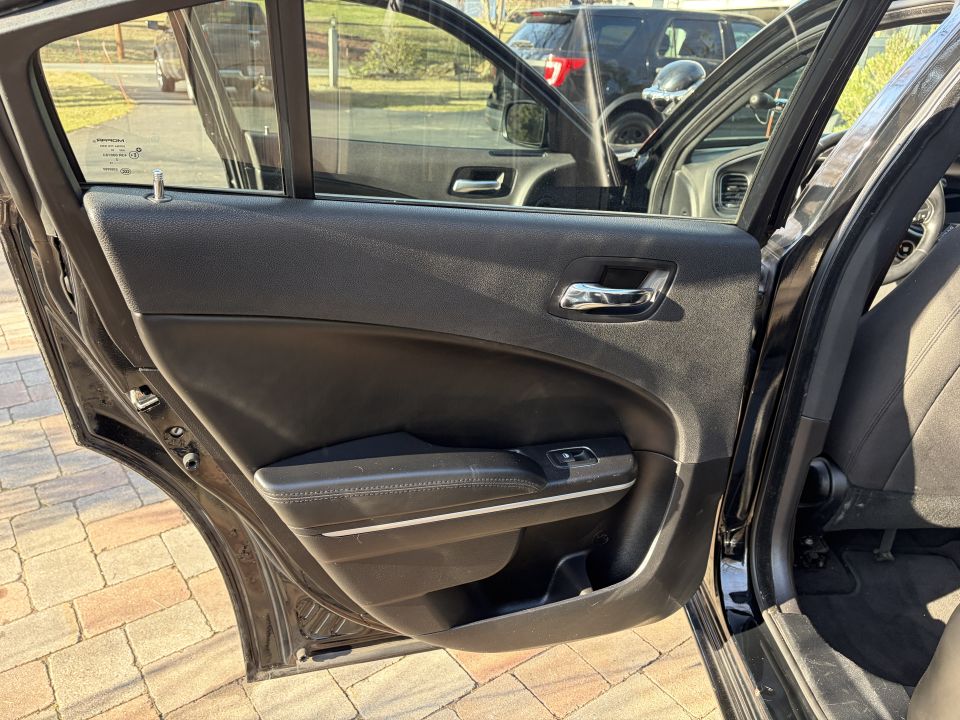 Shot of a black Dodge Charger's interior, showing the driver's side door panel and seat. Another SUV is visible through the open door