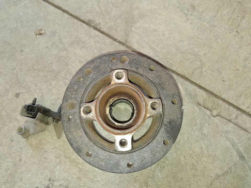 Crankshaft pulley with a sensor attached, lying on a concrete surface