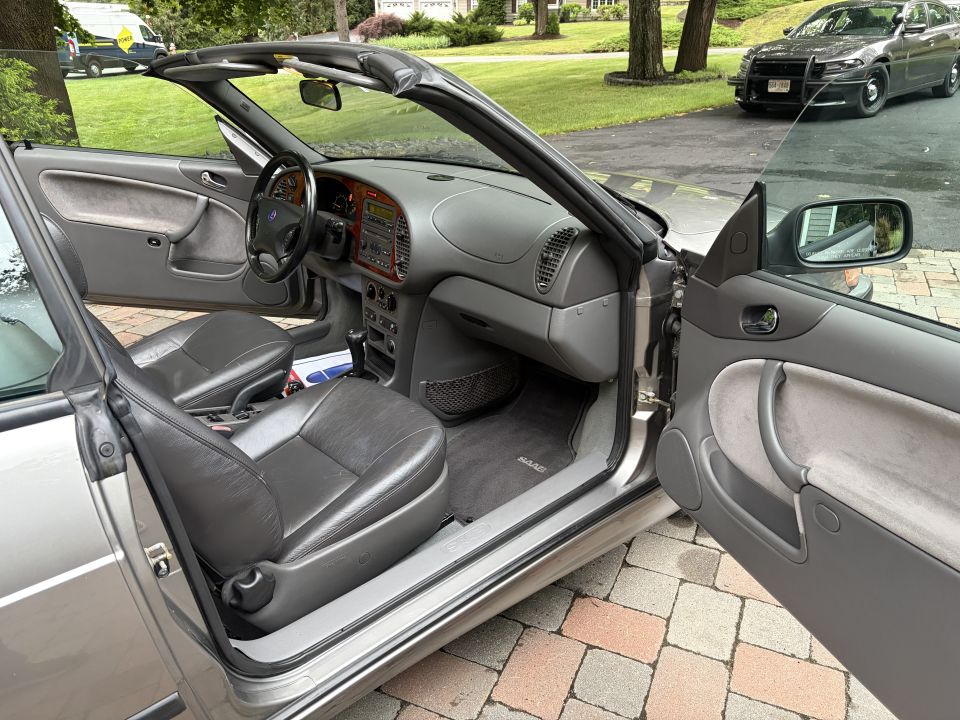 Silver Saab convertible interior with door open, gray leather seats and wood-trim dash
