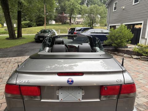 2001 Ford Crown Victoria - Rear view of a silver-gray Saab 9-3 convertible with the soft top down, parked on a brick-paver driveway. The trunk lid wears 'SAAB' and '9…