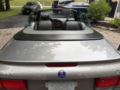2001 Ford Crown Victoria - Rear three-quarter view of a silver-gray Saab 9-3 convertible with the top down, parked on a brick paver driveway; the trunk lid shows the…