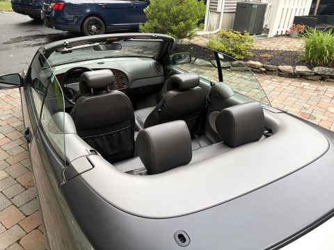 2001 Ford Crown Victoria - Overhead view into the cabin of a convertible with the top down, showing dark leather front seats and rear headrests behind a clear plastic…