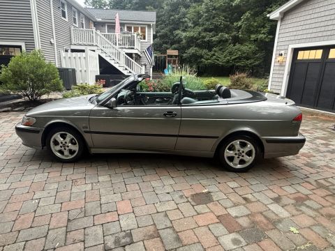 2001 Ford Crown Victoria - Driver-side profile of a gray convertible with the top down, parked on a brick paver driveway in front of a gray house and garage. It rides…