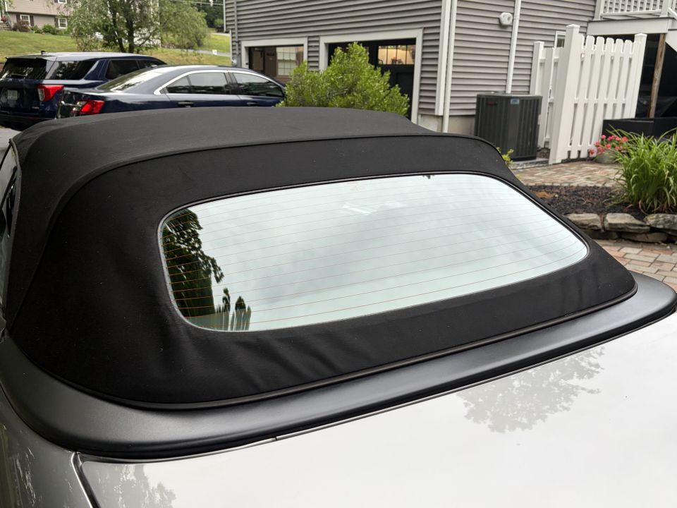 Black convertible soft-top with glass rear window over silver rear body panel