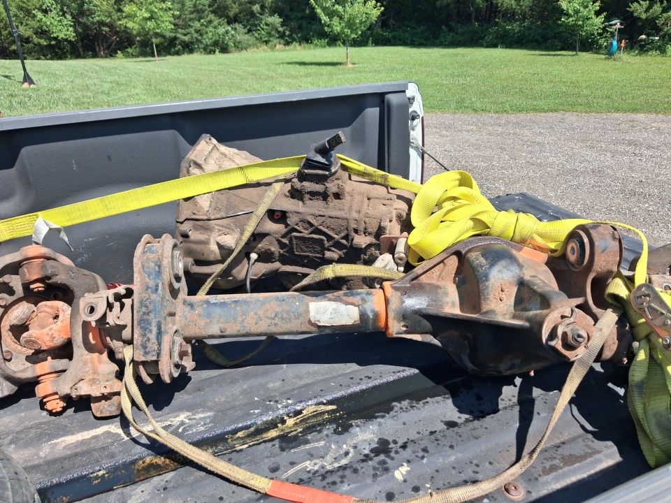 Rusty axle, differential and transfer case strapped in a truck bed