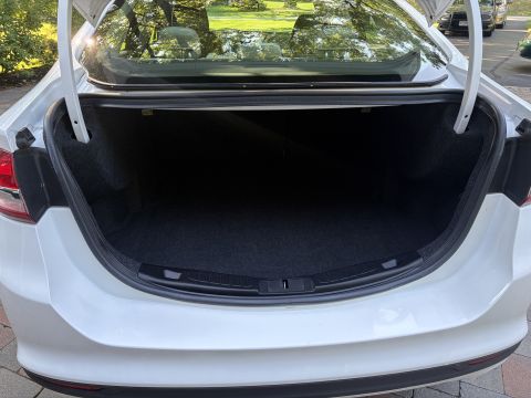 2001 Ford Crown Victoria - Open trunk of a white sedan showing the empty black carpeted cargo area, rear parcel shelf, and taillight housings from behind.