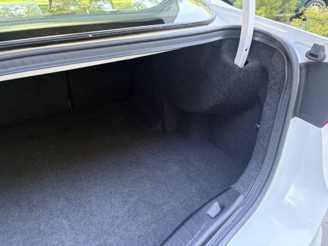 2001 Ford Crown Victoria - Open trunk of a white sedan showing the empty carpeted cargo area, dark trunk liner and hinge, photographed outdoors.