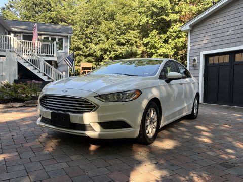 2001 Ford Crown Victoria - White Ford Fusion sedan viewed from the 3/4 front driver side on a paver driveway, showing the mesh grille with Ford oval and projector hea…