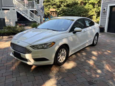 2001 Ford Crown Victoria - Front three-quarter view of a white Ford Fusion sedan on a paver driveway, its Ford oval badge and chrome-bar grille facing the camera. A s…