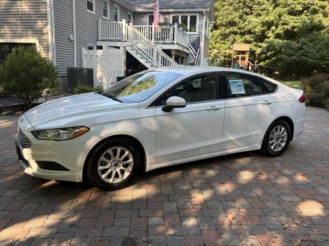 2001 Ford Crown Victoria - White Ford Fusion sedan viewed from the 3/4 front on a paver driveway, with dealer window stickers still in the glass and a Ford oval on th…