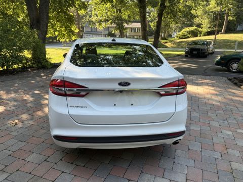 2001 Ford Crown Victoria - Rear view of a white Ford Fusion sedan on a paver driveway, showing the 'Fusion' script and Ford oval badge, a chrome trim bar across the t…