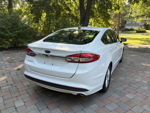 2001 Ford Crown Victoria - White Ford Fusion sedan shown from the 3/4 rear on brick pavers, showing the Ford-badged trunk, wraparound taillights, and single exhaust o…