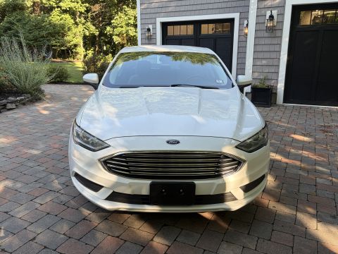 2001 Ford Crown Victoria - Head-on front view of a white Ford Fusion sedan parked on a brick paver driveway, showing the mesh grille with the Ford oval badge and an e…