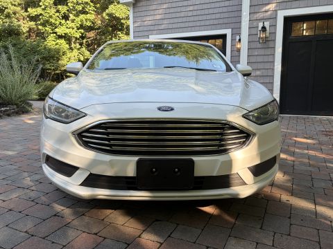 2001 Ford Crown Victoria - Head-on front view of a white Ford Fusion sedan, showing the Ford oval on the hood, a horizontal-bar chrome grille, and the front plate bra…