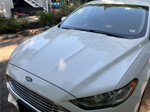 2001 Ford Crown Victoria - Close-up of the hood and front end of a white Ford sedan, showing the chrome-slat grille with a blue Ford oval, headlight and windshield wi…
