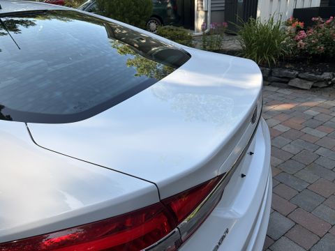 2001 Ford Crown Victoria - Close-up of the rear decklid, spoiler lip and taillight of a white Ford Fusion sedan, with the rear glass and a brick driveway visible.