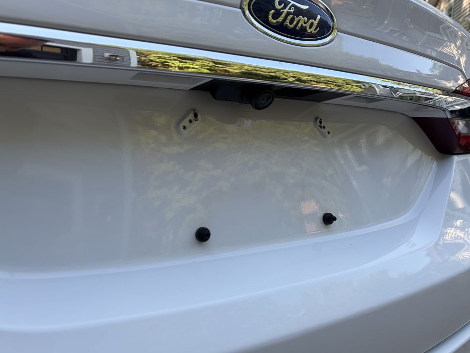 Close-up of white Ford trunk badge, backup camera and plate mounting holes