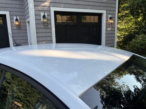 2001 Ford Crown Victoria - Close-up of the white painted roof and A-pillar of a sedan, showing the glossy paint and trim, with a gray shingled house and garage doors…
