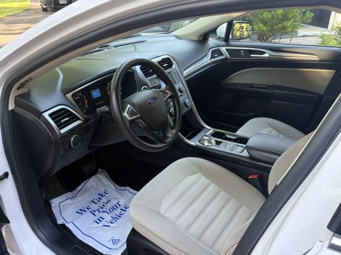 2001 Ford Crown Victoria - Interior view of a Ford sedan through the open driver's door, showing the black steering wheel with Ford emblem, tan cloth front seats, and…