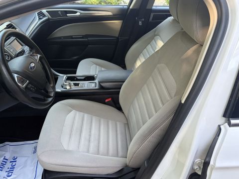 2001 Ford Crown Victoria - Front seat interior of a white sedan shot from the passenger door, showing light gray/tan cloth front seats, a black leather Ford steering…