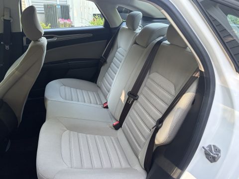 2001 Ford Crown Victoria - Rear bench seat of a white sedan upholstered in light stone cloth, with the door open and dark seatbelts draped across the seat. Air-condit…