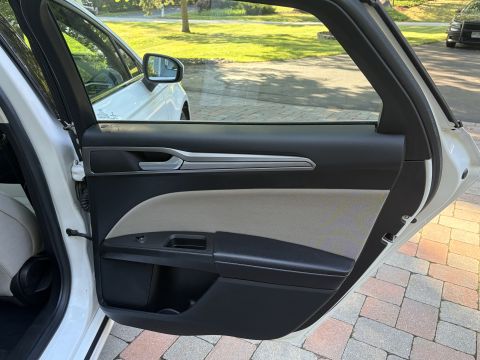 2001 Ford Crown Victoria - Open rear door of a white sedan showing the black and light-stone door panel with armrest and switches, and the interior seat edge. A brick…