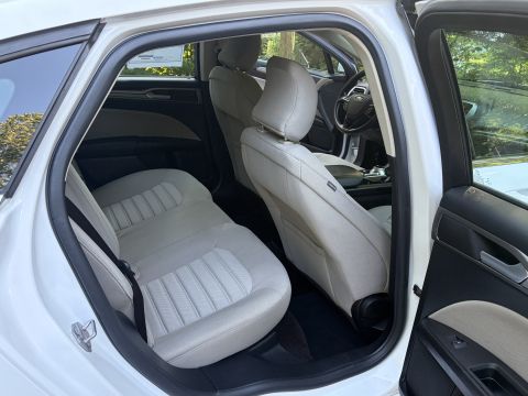 2001 Ford Crown Victoria - Rear passenger compartment of a white Ford sedan shown through the open rear driver-side door, with light beige/tan cloth seats and dark ca…