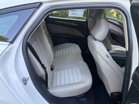 2001 Ford Crown Victoria - Rear seat area of a white sedan seen through the open rear door, with light tan cloth bench and seatbacks and a window sticker taped to the…