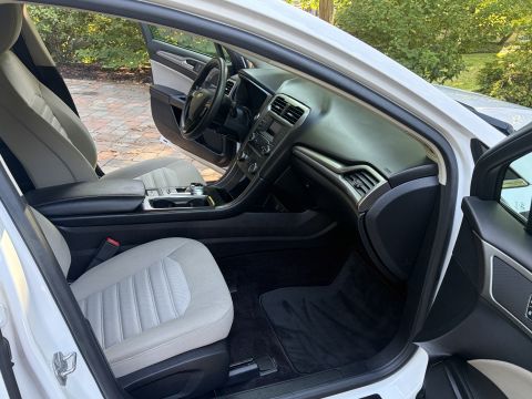 2001 Ford Crown Victoria - Interior of a white Ford Fusion viewed from the open passenger door, showing the dashboard, rotary shifter center console and tan cloth fro…