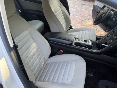 2001 Ford Crown Victoria - Front seats of a white Ford sedan viewed from the passenger side, with light tan cloth upholstery, black leather center armrest, cupholders…