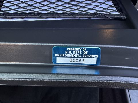 2001 Ford Crown Victoria - Close-up of a blue metal asset tag reading "PROPERTY OF N.H. DEPT. OF ENVIRONMENTAL SERVICES" with white number strip 32066, affixed to a b…