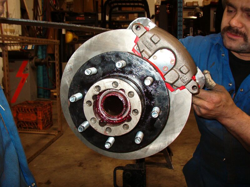 Mechanic installing brake caliper on greased hub and rotor assembly
